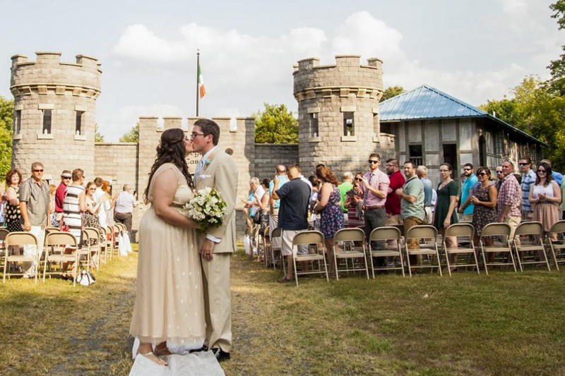 A bride and groom kissing in front of a castle and a crowd of people at their seats