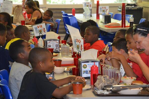 Young scouts and their leader eating hamburgers around a table in a dining hall