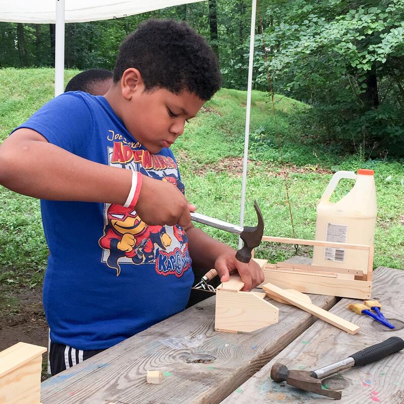 A boy hammers a nail into the wooden toolbox he is building