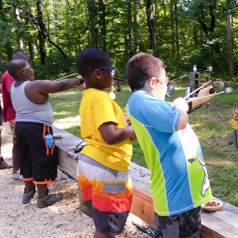 Four young scouts shooting slingshots