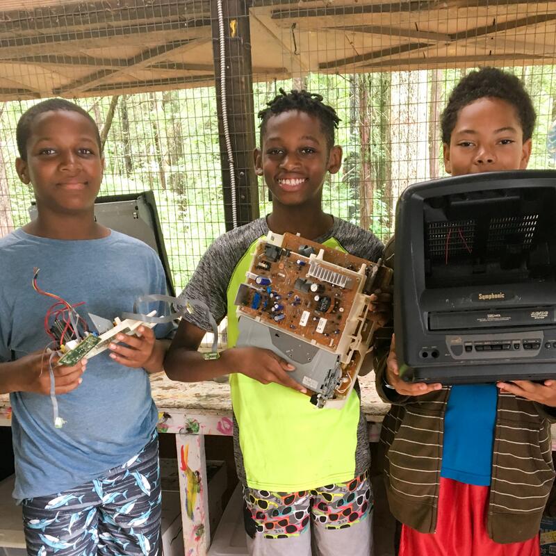 Three boys hold up parts of a small disassembled television